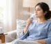 Person using a nebulizer with a mouthpiece while sitting on a sofa at home