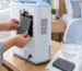 Hands removing a washable gray foam filter from a home oxygen concentrator for cleaning