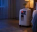 Oxygen concentrator with a red warning light glowing beside a bed in a softly lit bedroom at night